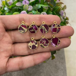 May include: Seven circular pendants with a gold-coloured frame. The pendants display a deep red and gold-coloured stone with a distinctive, textured design. Each pendant has a small loop at the top for attaching to a chain or other jewellery component.