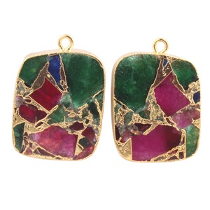Puede incluir: Un par de colgantes cuadrados de tono dorado con una incrustación de piedra multicolor y multifacética. La piedra presenta tonos de verde, rojo y azul, con motas doradas.