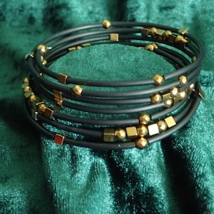 Könnte beinhalten: Ein schwarzes und goldenes Armband aus mehreren dünnen Bändern mit goldenen Perlen und quadratischen Akzenten.