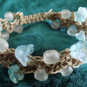 Könnte beinhalten: Ein geflochtenes Armband mit hellblauen und weißen Glasperlen. Das Armband ist aus braunem Kordel gefertigt und hat ein schlichtes Design.