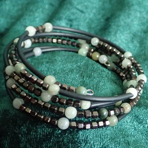 May include: A multi-strand bracelet featuring green and white beads, along with silver-toned metal beads. The bracelet is made of elastic and is designed to be worn on the wrist.