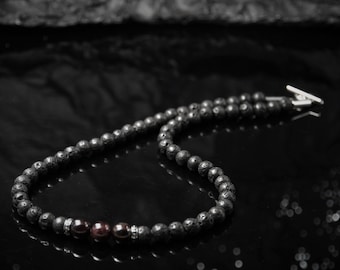Könnte beinhalten: Eine schwarze Lava-Perlenkette mit drei roten Granatperlen und silbernen Akzenten.