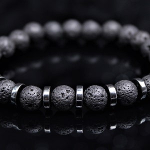 Könnte beinhalten: Ein schwarzes Lava-Armband mit silbernen Metallperlen. Das Armband besteht aus natürlichem Lavastein und silbernen Metallperlen.