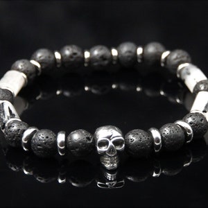 Könnte beinhalten: Ein Armband aus schwarzen Lavasteinen mit silbernen Zwischenstücken und einem silbernen Totenkopf-Anhänger.