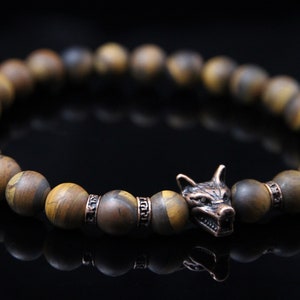 May include: A brown and gold beaded bracelet with a wolf head charm. The beads are made of tiger's eye stone.