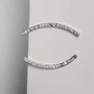 Puede incluir: Un par de pendientes de plata con un dise&ntilde;o texturizado y curvo.