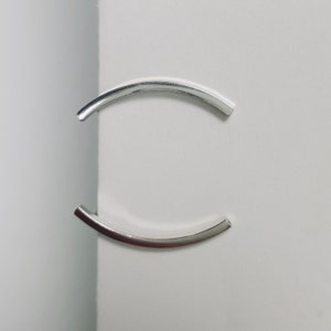 Puede incluir: Dos anillos de metal plateado, cada uno con forma de semic&iacute;rculo, se colocan sobre una superficie blanca para formar un c&iacute;rculo completo.