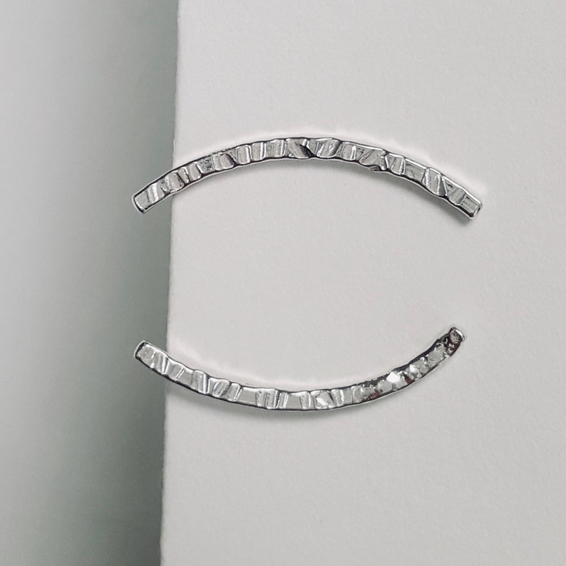 Puede incluir: Un par de pendientes de plata con un dise&ntilde;o texturizado y curvo.