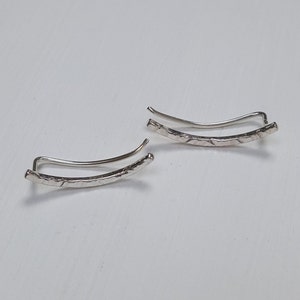 Puede incluir: Un par de pendientes de plata con acabado texturizado. Los pendientes son curvos y tienen un dise&ntilde;o sencillo.