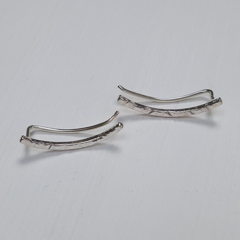 Puede incluir: Un par de pendientes de plata con acabado texturizado. Los pendientes son curvos y tienen un dise&ntilde;o sencillo.