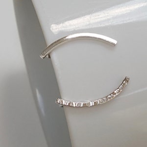 Puede incluir: Un par de pendientes de aro de plata. Un aro es liso y el otro tiene una superficie texturizada.