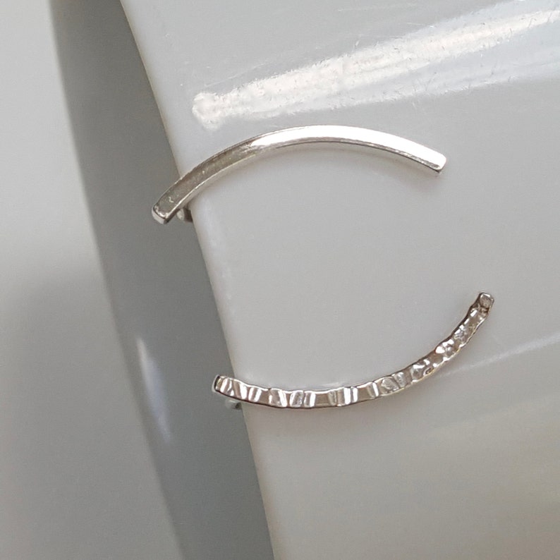 Puede incluir: Un par de pendientes de aro de plata. Un aro es liso y el otro tiene una superficie texturizada.