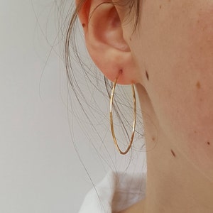 May include: A pair of gold hoop earrings with a hammered texture. The earrings are worn in a person's ear.