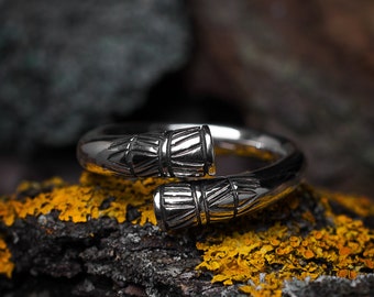 May include: A silver ring with a unique design featuring two intertwined, textured bands. The ring is resting on a piece of bark with yellow lichen.