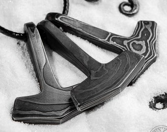 May include: Three silver-colored metal pendants shaped like hammers with intricate patterns on the surface. The pendants are hanging on a black cord.