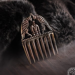 May include: A gold-toned comb with a decorative design of two birds flanking a central figure. The comb has seven teeth and is set against a dark background.