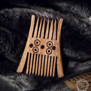 May include: A wooden comb with a unique design featuring multiple rows of teeth and circular cutouts. The comb is brown and has a natural wood finish.