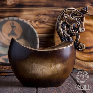 May include: A wooden bowl with a carved dragon head handle. The bowl is dark brown with a light brown wood grain. The dragon head is detailed with scales and a curled tail.