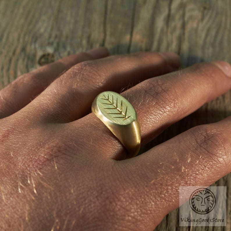 May include: A gold signet ring with an oval-shaped top featuring a stylised leaf design.