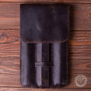 May include: A brown leather case with three slots for holding pens or pencils. The case has a flap that closes with a strap.