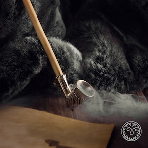 Pode incluir: Um cachimbo de madeira com uma tigela de metal e um longo caule. O cachimbo está sobre uma superfície marrom e está cercado por fumaça.