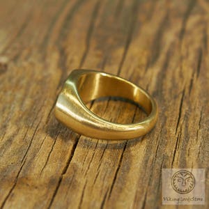May include: A gold signet ring with a smooth, rounded surface. The ring is made of metal and has a simple, classic design.