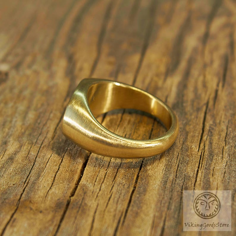 May include: A gold signet ring with a smooth, rounded surface. The ring is made of metal and has a simple, classic design.