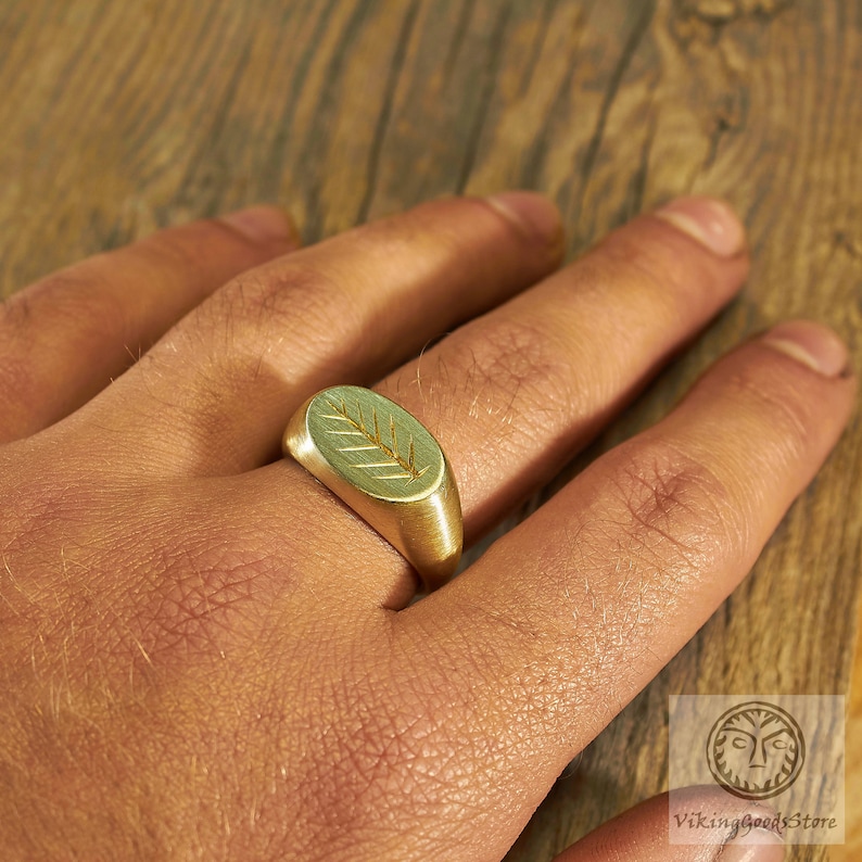 May include: A gold ring with a leaf design on the top. The ring is worn on a person's finger.