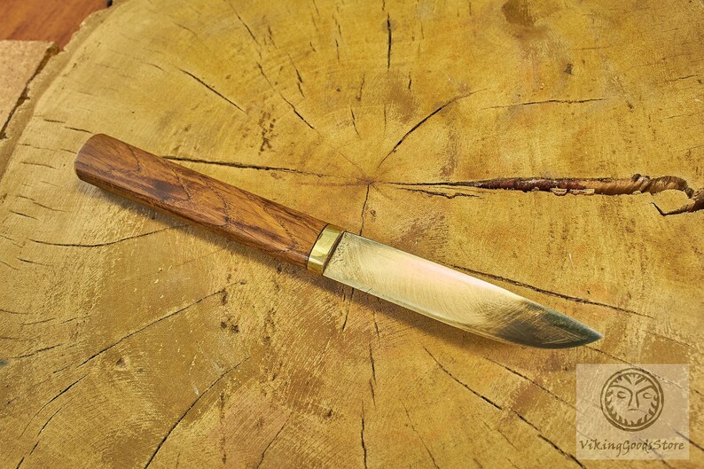 Puede incluir: Un cuchillo con mango de madera y hoja de lat&oacute;n, que se encuentra sobre una superficie de madera.