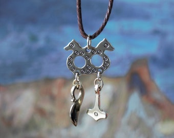 May include: A silver pendant necklace with a double-headed serpent design, with a small silver hammer and a silver blade pendant hanging from it. The necklace is on a brown cord.
