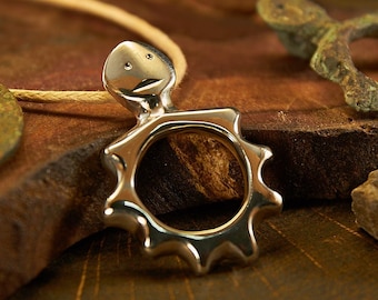 May include: Silver pendant necklace with a sun-shaped design and a small face on top. The pendant is on a brown wooden surface.