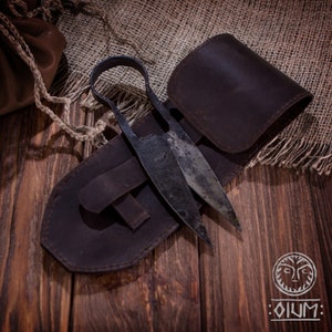 Könnte beinhalten: Eine antike Schere mit einer braunen Lederscheide. Die Schere hat ein rustikales, gealtertes Aussehen und ist aus Metall. Die Scheide hat eine Klappe, die die Schere sichert.