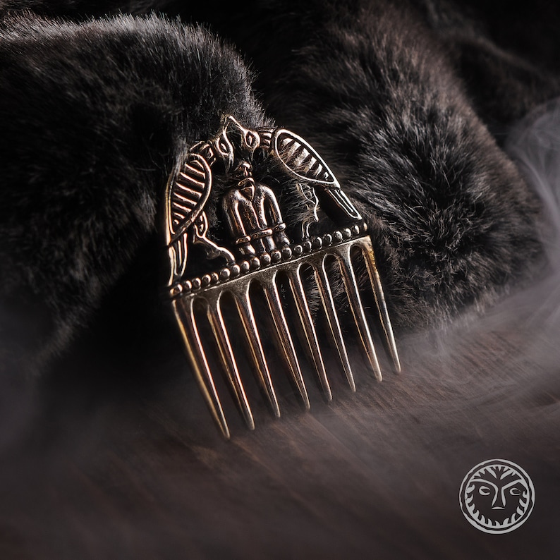 May include: A gold-toned comb with a decorative design of two birds flanking a central figure. The comb has seven teeth and is set against a dark background.