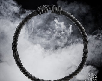 May include: A black metal ring with a twisted design, photographed against a white smoky background.