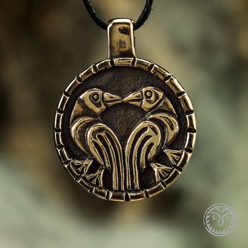 May include: A gold-toned pendant necklace featuring a circular design with two stylized birds facing each other. The birds are intricately detailed and have their beaks touching.