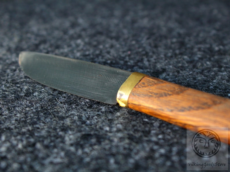 Puede incluir: Primer plano de un cuchillo peque&ntilde;o con mango negro y una virola de lat&oacute;n. La hoja es de acero y tiene un borde ligeramente curvado. El mango es de madera y tiene un acabado marr&oacute;n oscuro.