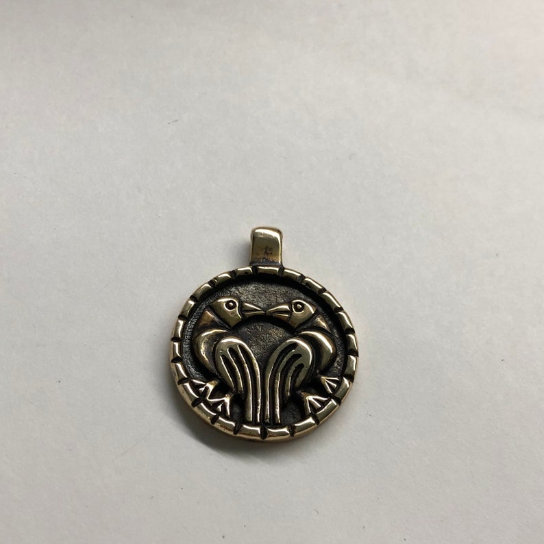 May include: A gold-toned pendant featuring two stylized birds facing each other with their beaks touching. The pendant is circular and has a detailed design.