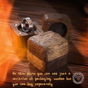 K&ouml;nnte beinhalten: Eine Holzschachtel f&uuml;r Ringe mit einem silbernen Ring im Inneren. Die Schachtel ist aus dunklem Holz mit einem hellen Holzrand. Die Schachtel steht auf einer Holzoberfl&auml;che.