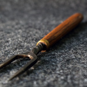 Op de afbeelding: Een metalen vork met een houten handvat en een gedraaide metalen schacht. De vork heeft drie tanden en een gouden band aan de bovenkant van het handvat.