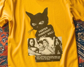 May include: Mustard yellow t-shirt with a black cat graphic and the text "FASTER PUSSYCAT! KILL! KILL!". Underneath the cat is a collage of vintage images with the text "FULL BOSOMED BEAUTIES WHO CAN NOT ONLY BREAK YOUR HEART BUT YOUR NECK AS WELL".
