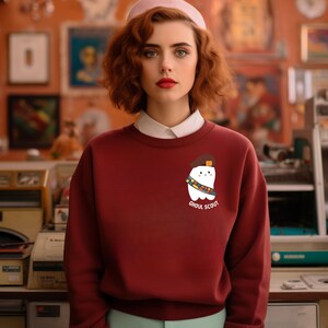 May include: A maroon sweatshirt with a white ghost wearing a scout hat and sash. The text "Ghoul Scout" is printed below the ghost.