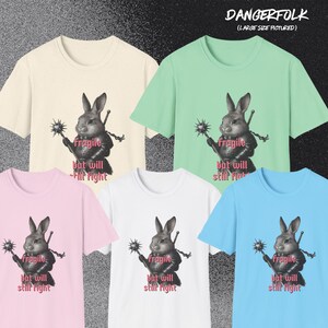 K&ouml;nnte beinhalten: Verschiedene T-Shirts in Creme, Mintgr&uuml;n, Rosa, Wei&szlig; und Hellblau. Jedes Shirt zeigt eine Grafik eines Kaninchenkriegers mit dem Text "Fragile but will still fight". Der Markenname "DANGERFOLK" ist sichtbar.