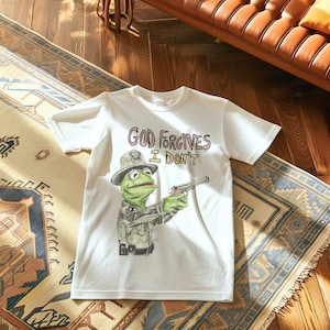 May include: White t-shirt with a green Muppet character holding a gun. The text on the shirt reads "God Forgives I Don't".