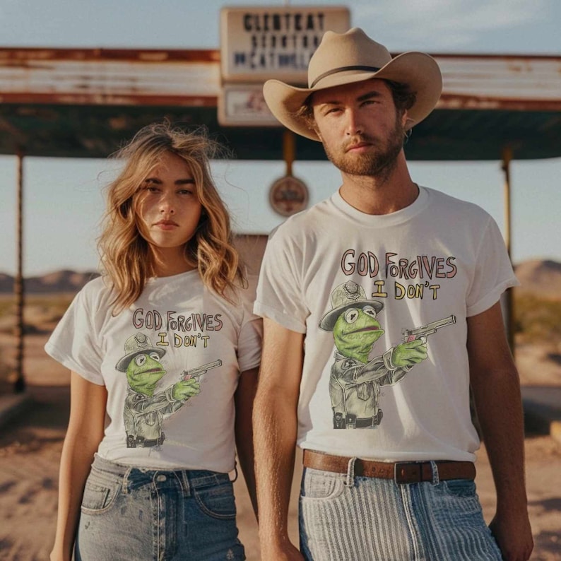 May include: Two people wearing white t-shirts with a green Muppet character holding a gun and the text "God Forgives I Don't". The person on the left is wearing blue jeans and the person on the right is wearing a brown cowboy hat and striped blue jeans.