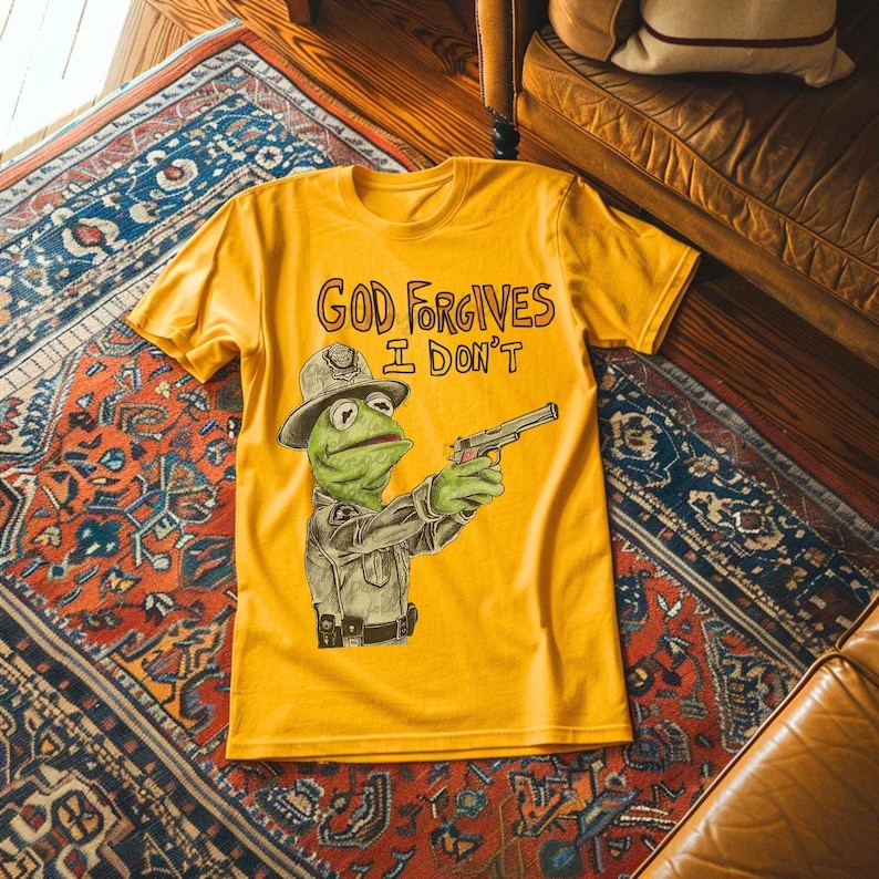May include: A yellow t-shirt with a cartoon image of a green frog wearing a police hat and holding a gun. The text "GOD FORGIVES I DON'T" is printed on the shirt.