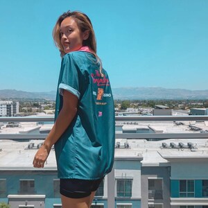 May include: A teal blue bowling shirt with a pink and white design on the back. The design includes the text "The Ringmaster" and "Hotel Casino".