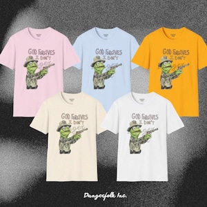 May include: Five t-shirts in different colors with a graphic of a green frog wearing a ranger hat and holding a gun. The text on the shirts reads "God Forgives I Don't".