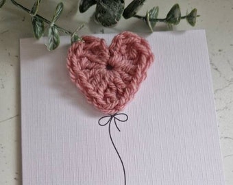 May include: A white card with a pink crocheted heart balloon and the text "Welcome to the world beautiful you".