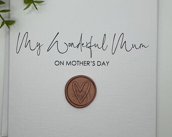 May include: A white card with black text that reads "My Wonderful Mum on Mother's Day". A rose gold wax seal with a heart design is in the lower center of the card.