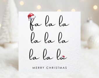 May include: A white card with the text "Fa la la la" repeated three times in black script, with small Santa hats. The words "Merry Christmas" are printed below. Festive holiday card.
